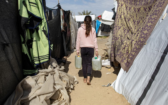 Ein palästinensisches Mädchen trägt zwei Wassercontainer in einem Zeltlager für Binnenvertriebene in Gaza.