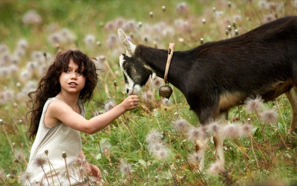 映画のワンシーン：ヤギと山の花畑にいるハイジ