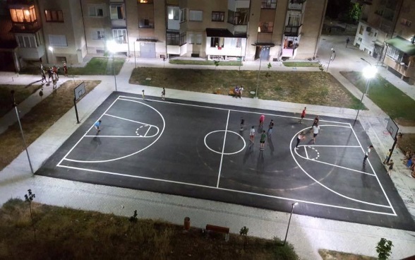 Jugendliche spielen am Abend auf einem beleuchteten Basketballfeld.