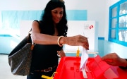 Eine junge Frau wirft einen gefalteten Wahlzettel in eine Wahlurne.