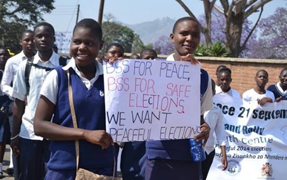 Une jeune femme et un jeune homme brandissent une affiche qui proclame «We want peaceful elections», en français: «Nous voulons des élections pacifiques».