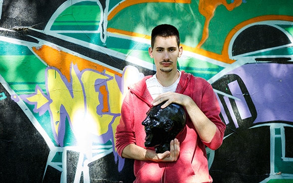 Stefan, 24 anni, davanti a un muro coperto di graffiti.