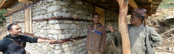 Un muratore parla con due abitanti di un villaggio davanti a un’abitazione ristrutturata.  