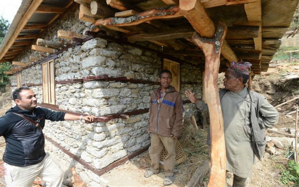 Ein Maurer unterhält sich vor einem wieder aufgebauten Haus mit zwei Dorfbewohnern.