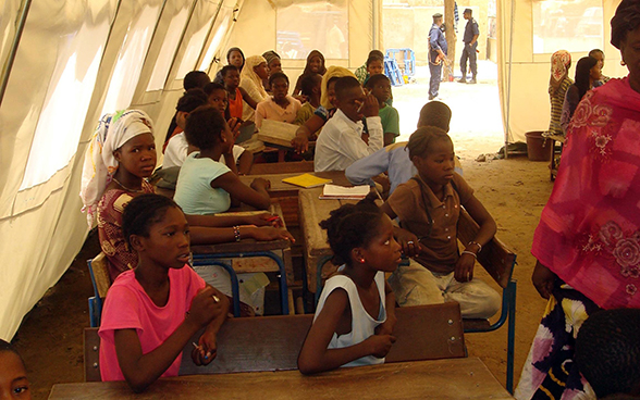 Bambini seduti ai loro banchi di scuola sotto una tenda.