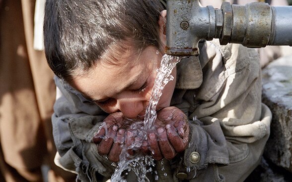Un ragazzo in Afghanistan beve acqua da una fontana.