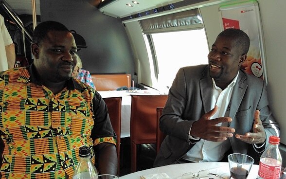 Ambroise Tapsoba e Issa Compaoré discutono seduti nella carrozza ristorante di un treno delle FFS.