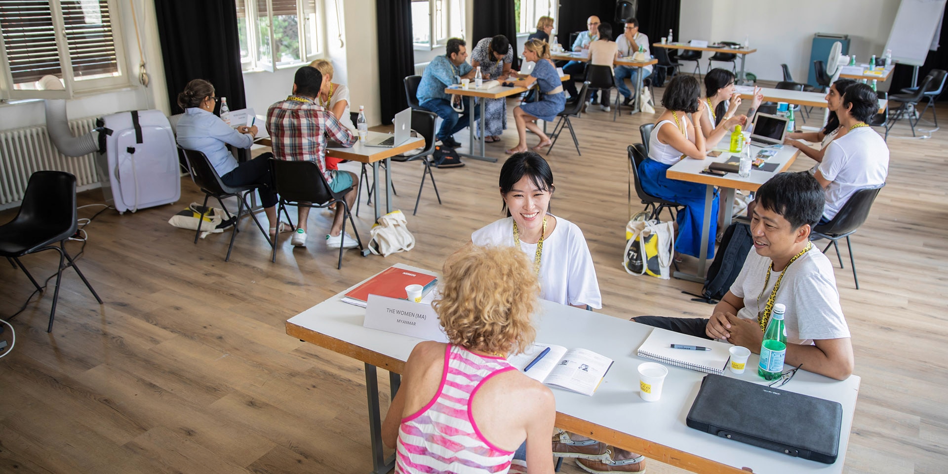 In una sala alcuni giovani stanno lavorando a gruppi, seduti attorno a dei tavoli.