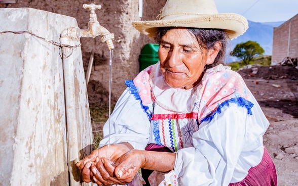 Una donna boliviana si lava le mani a una fontanella.