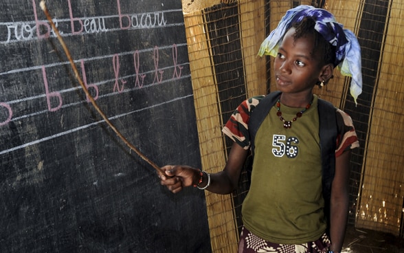 Une fillette d'une école nomade au Mali debout devant un tableau noir.