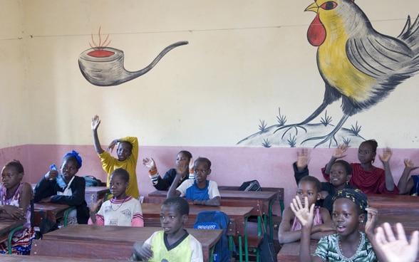 Une classe d'école au Mali pose devant un mur peint de couleurs vives. 