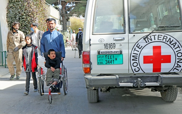 Persone che si recano in un ospedale afghano accanto a un veicolo del CICR.