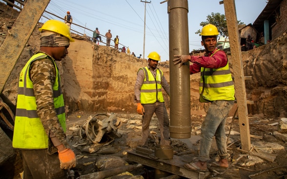 In un cantiere attivo per la costruzione di un ponte, tre operai vengono fotografati al lavoro.