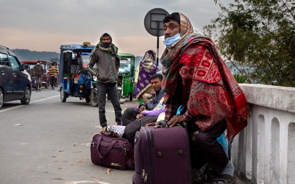 Sul ciglio di una strada, alcune persone attendono con le loro valigie.