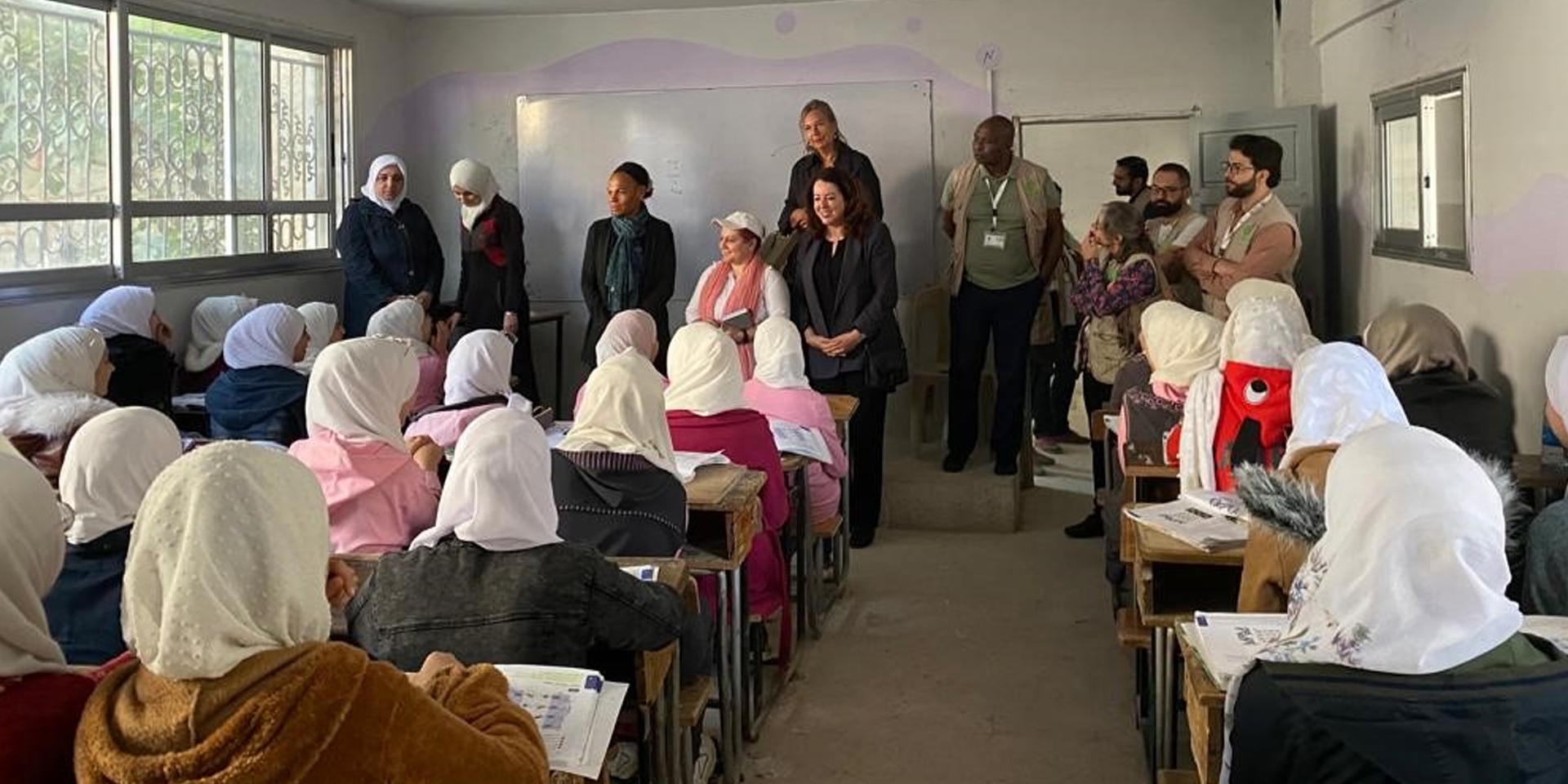 Escuela de niñas en Siria. Entre otras personas, puede verse a la directora de la COSUDE, Patricia Danzi, y a la embajadora Maya Tissafi de pie delante de una pizarra mientras hablan con las alumnas.