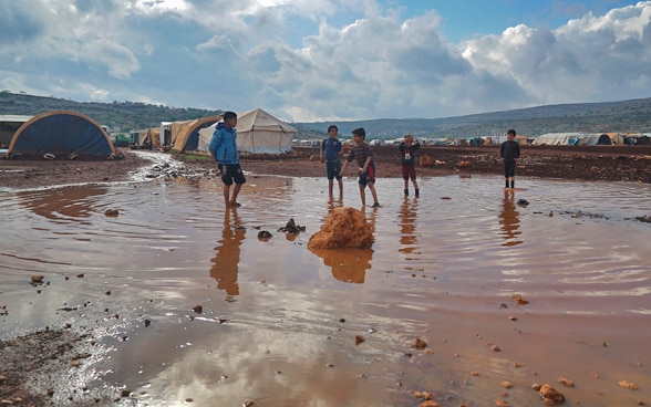 Children in the camp for internally displaced persons "Kafr Aruq" play in a large rain puddle.