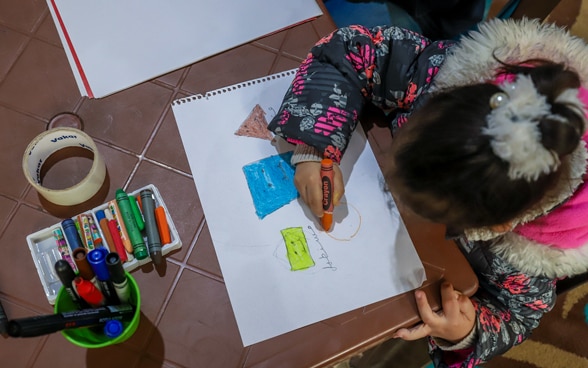 Une fillette dessine un cercle sur une feuille de papier avec de la peinture orange.