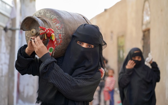 Due donne portano una bombola di gas in spalla e vanno a cercare gas al mercato nero.