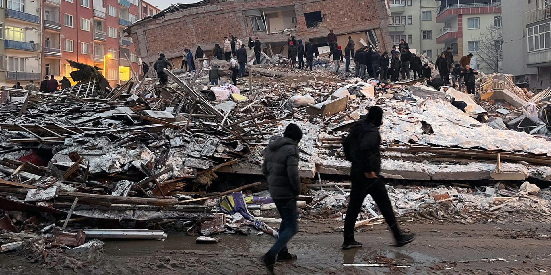 Molte persone in piedi davanti alle macerie di un edificio crollato.