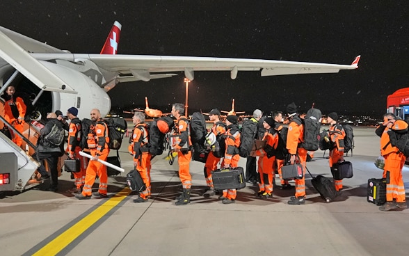 Une dizaine de membres de la Chaîne de sauvetage se tiennent devant les escaliers menant à l'avion.