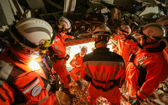  Six members of Swiss Rescue stand talking in the rubble of a building.