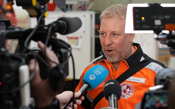 The operations manager of Swiss Rescue, Sebastian Eugster, speaking to the media, surrounded by microphones and cameras. 