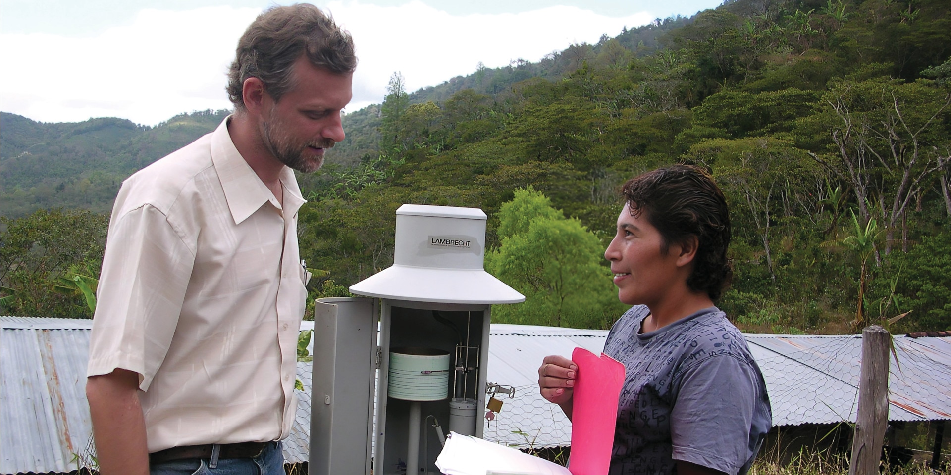 A man and a woman talking outside by a climate monitoring station.