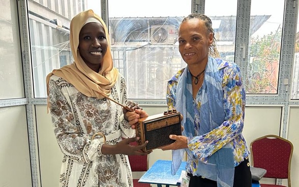 DEZA-Direktorin Patricia Danzi steht neben einer jungen tschadischen Journalistin, Hawa Mahamat Adouma, von Radio Ndarason, und hält ein Transistorradio in den Händen.