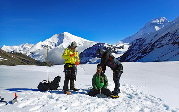 Drei Forscher entnehmen in einem verschneiten Berggebiet Eisproben.