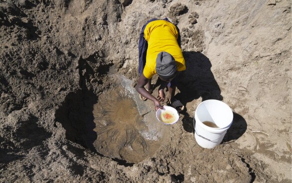Una lugareña recoge agua de un agujero en el suelo.