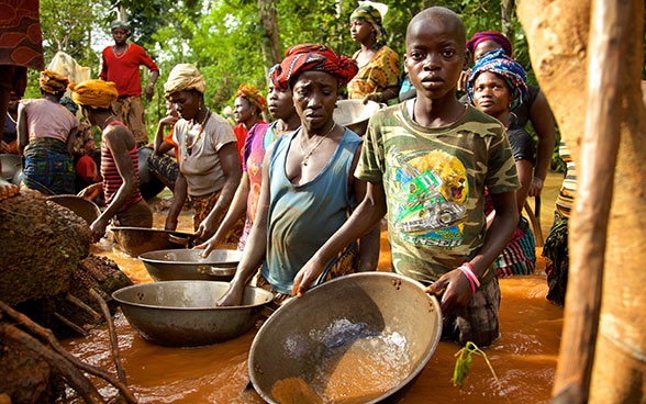 Frauen, Männer und Kinder aus einem Dorf in Sierra Leone, die hüfttief im Wasser stehen und versuchen, das geschürfte Gold von Verunreinigungen zu befreien.