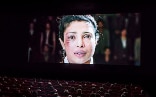 Le visage d’une femme est projeté sur l’écran d’une salle de cinéma. Elle a une blessure près de l'œil gauche et pleure.