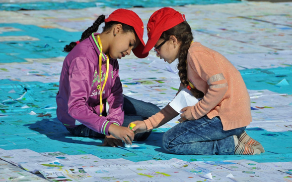 Deux fillettes marocaines collent des cartes agenouillées sur le sol.
