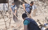 Three men in Syria shovelling rubble from collapsed buildings into heaps.