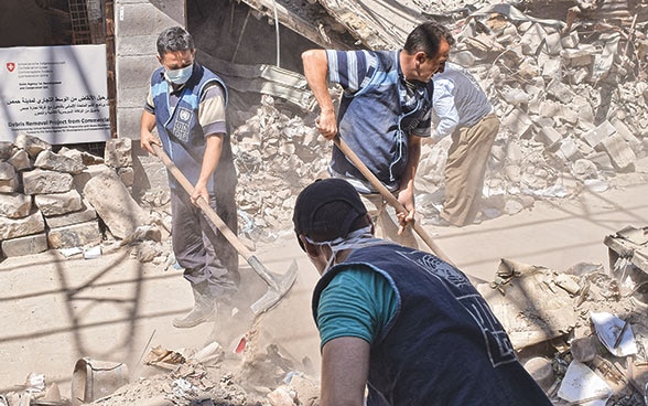 Siria: tre uomini al lavoro con le pale per rimuovere pietre e macerie.