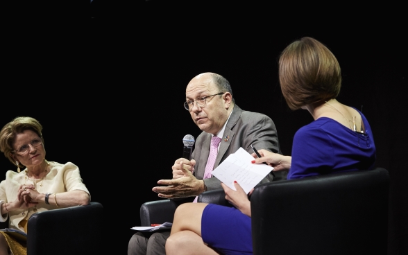 Marie-Gabrielle Ineichen-Fleisch e Melanie Pfändler siedono sul palco e ascoltano con attenzione Thomas Gass, seduto tra di loro, mentre parla al microfono.