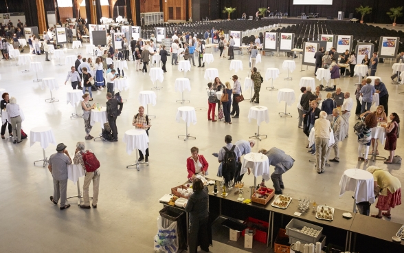 Die Festhalle der Bernexpo von oben: An vielen kleinen Stehtischen stehen Teilnehmende, sie unterhalten sich, trinken oder essen etwas.