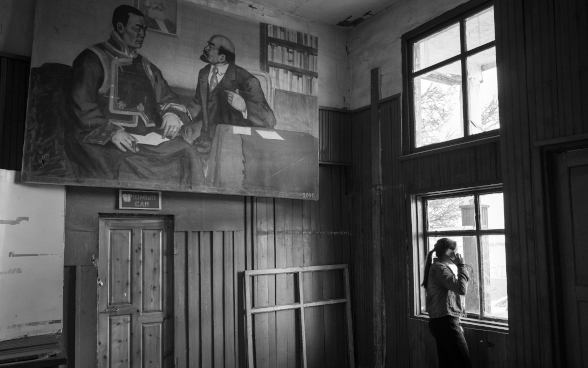 A young woman standing at a window, talking on a smartphone.