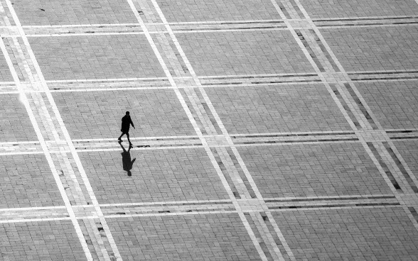 Silhouette of a person walking across a square.