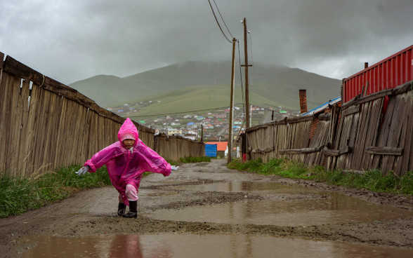Bambina che cammina sotto la pioggia in una strada fangosa nel quartiere delle yurte di Ulan Bator.