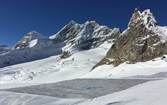 Die grösste Postkarte der Welt auf dem Gletscher, im Hintergrund sind Berge zu sehen. 