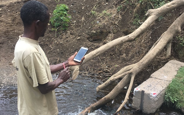 Ein Kleinbauer im Einzugsgebiet des Pangani Flusses in Tanzania misst mit seinem Smartphone die Abflussmenge in einem Bewässerungskanal.