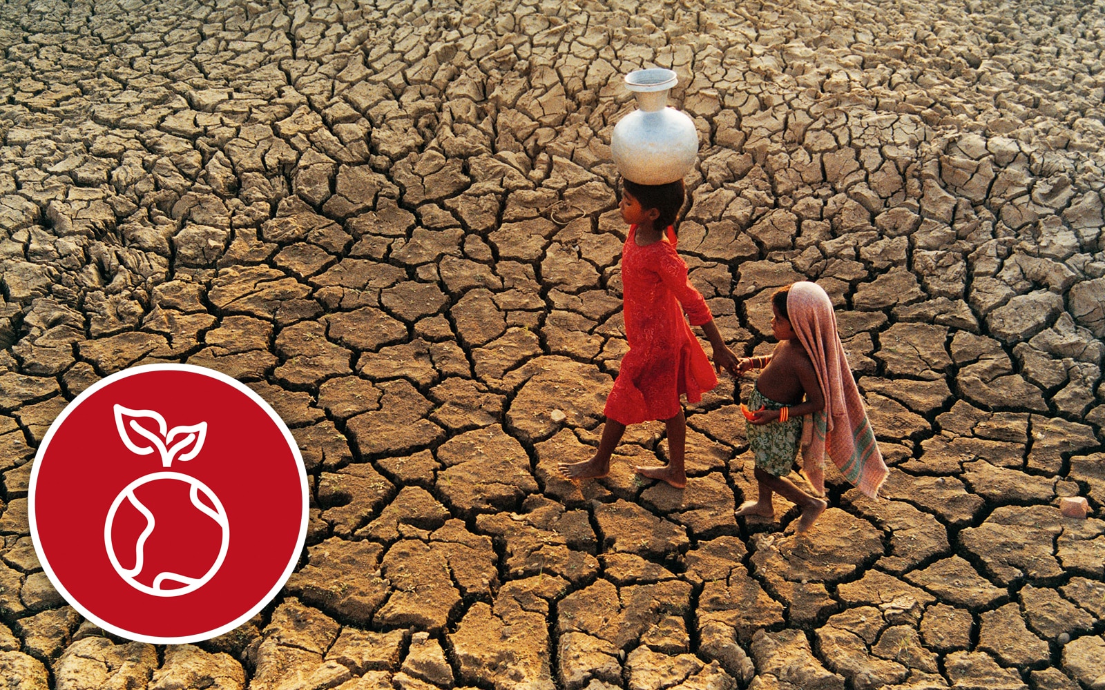  Two children walk across a dried-out river bed with a pitcher of water.