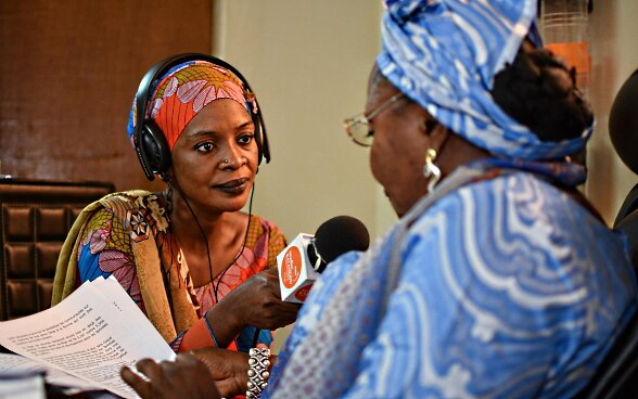 In uno studio radiofonico, una donna africana invervista un’altra donna tendendole un microfono.