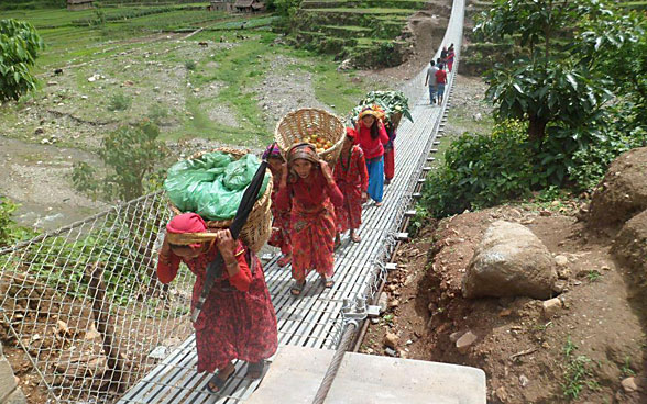 Frauen mit Tragkörben begehen eine Fussgängerbrücke.