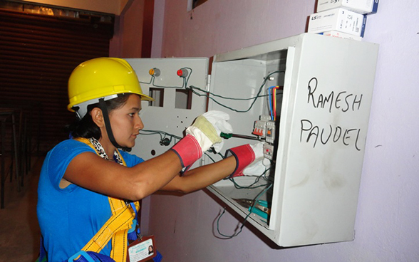 Eine junge nepalesische Frau arbeitet an einem Sicherungskasten. 