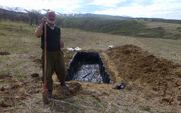 Un contadino del Tagikistan vicino a una fossa scavata per raccogliere acqua piovana.