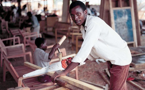 A young man sawing a wooden board.