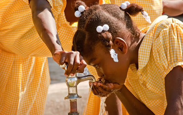 Ein Mädchen trinkt Wasser aus einem Wasserhahn