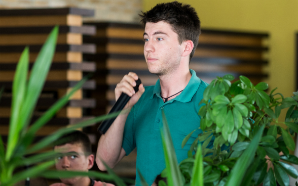 Ein junger Herr hält ein Mikrofon in der Hand und hört der Diskussion gebannt zu.